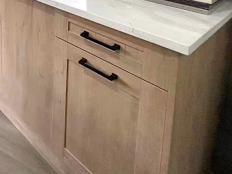 Natural oak shaker drawer and door with matte black bar pulls under a white quartz counter.