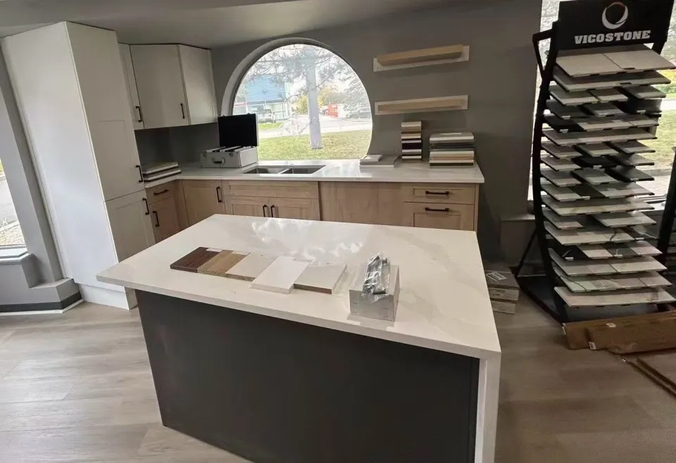 The T&F showroom: a display kitchen with white and natural oak shaker cabinets, a quartz waterfall island, the round window and a Vicostone quartz rack.